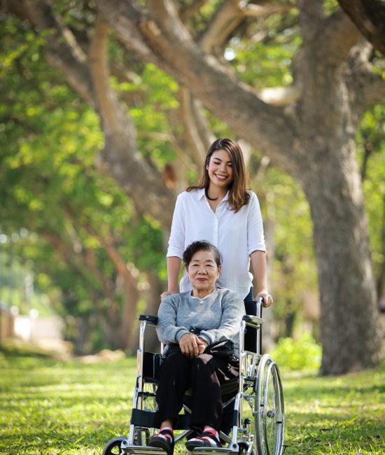 Asian senior woman sitting on the wheelchair with her daugther f Asian senior woman sitting on the wheelchair with her daugther family happy smile face on the green park